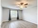 An empty bedroom with wood-look floors, a ceiling fan, neutral walls, and a window with black curtains at 9376 Se 175Th Pompion St, The Villages, FL 32162