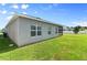 View of the backyard featuring lush green grass, gray stucco walls, and an enclosed screened-in patio at 410 Winter Bliss Ln, Mount Dora, FL 32757