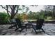 An outdoor stone patio with a fire pit and three black chairs surrounded by lush greenery and a wooden fence at 610 Cypress Ave, Orange City, FL 32763