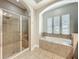 Bright bathroom featuring a tiled shower with glass door and a large soaking tub with three windows at 6971 Tettenhall Ln, Windermere, FL 34786