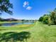 Scenic backyard view showing pond, lush green grass, and other homes in the distance under a sunny sky at 12832 Sawgrass Pine Cir, Orlando, FL 32824