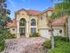 Exterior view of a tan two-story home with a red brick driveway and tropical landscaping at 2209 Callaway Ct, Davenport, FL 33837