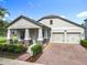 Charming one-story home featuring a two-car garage, brick driveway, covered front porch with stone-clad columns, and manicured landscaping at 8030 John Hancock Dr, Winter Garden, FL 34787