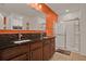 Bathroom featuring double sinks with black countertops, a glass shower, and an orange accent wall at 2216 Sequoia Way, Davenport, FL 33896