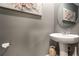 Stylish powder room features a pedestal sink, round mirror, gray walls, and elegant floral artwork at 3759 Crimson Clover Dr, Mount Dora, FL 32757
