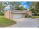 Tan home with a large driveway and attached two car garage surrounded by green grass and trees at 1102 Winter Springs Blvd, Winter Springs, FL 32708