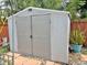 A gray, double-door shed sits on a paver base next to a blooming plant at 1428 Glendale St, Lakeland, FL 33803