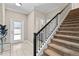 Bright foyer with staircase featuring neutral carpet and sleek, black railing, plus views of a nearby door and small nook at 2460 Reading Trl, Kissimmee, FL 34746
