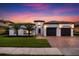 Mediterranean-style home at sunset boasts a two-car garage, vibrant landscaping, and decorative wrought iron gate for elegant appeal at 7733 Pointe Venezia Dr, Orlando, FL 32836