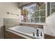 Soaking tub with tile surround beneath a sunny window with blind and curtain treatments at 1097 Harmony Ln, Clermont, FL 34711