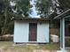 View of a shed with a brown door, surrounded by trees and an adjacent generator at 16320 3Rd St, Umatilla, FL 32784