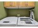 Close-up of white front-loading washer and dryer in laundry room with overhead wood cabinets at 1041 Cherry Valley Way, Orlando, FL 32828