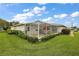 Home's rear exterior showcasing a screened patio, lush lawn, and well-maintained landscaping under a bright, cloudy sky at 1105 Apple Ter, Leesburg, FL 34748