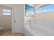 Bright bathroom featuring a soaking tub with white tile surround, arched window, and beach themed art at 141 Winsor Ave, Davenport, FL 33837