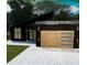 Modern home's unique exterior with dark siding, light wood garage doors, and sleek lighting at 5025 Sw 179Th Pl, Ocala, FL 34473
