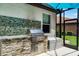 An outdoor kitchen features a grill, stone surround, and mosaic backsplash in the screened-in lanai at 100 Verde Way, Debary, FL 32713