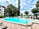 Community pool with red brick border with lounge chairs and landscaped trees under a cloudy sky at 1100 Delaney Ave # F407, Orlando, FL 32806