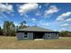 The backyard of a contemporary house featuring dark gray stucco walls, a gray shingled roof, and a spacious lawn at 4062 Sw 114Th St, Ocala, FL 34476