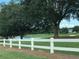 A scenic view of the golf course featuring a white fence, pond, and mature trees at 9994 Sw 96Th St, Ocala, FL 34481