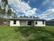 Exterior backyard view with sliding glass doors, a covered patio, green lawn and bordered by tall pines at 13374 Sw 63Rd Ter, Ocala, FL 34473