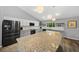 Bright kitchen featuring a large granite island, stainless steel appliances, and wooden floating shelves at 1934 Nw 79Th Loop, Ocala, FL 34475