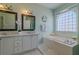 Bright bathroom features a double vanity, soaking tub with tile surround, and decorative mirrors at 15268 Sw 14Th Avenue Rd, Ocala, FL 34473