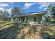 Green home features a covered patio with multiple windows and a spacious lawn, located near a paved road at 19662 Sw Marine Blvd, Dunnellon, FL 34431