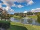 Scenic view of a tranquil pond with a fountain, lush greenery, and a clear blue sky with clouds at 5162 Harbour Dr, Oxford, FL 34484