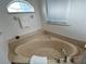 A close-up view of a tan corner bathtub next to a window with window blinds in the primary bathroom at 10923 Sw 38Th Ave, Ocala, FL 34476