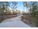 View of a single-story home with a gravel driveway, surrounded by tall pine trees and a blue sky at 11837 Se 165 Ave, Ocklawaha, FL 32179