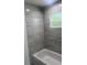 Modern bathroom featuring sleek gray wall tiles and a window over the tub at 14319 Se 26Th Ter, Summerfield, FL 34491