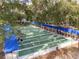 Aerial view of a well-maintained shuffleboard court with players, shaded seating, and lush trees at 10886 Sw 90Th Ter, Ocala, FL 34481