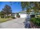 Well-maintained single-story home with a two-car garage, green lawn, and mature trees under a bright blue sky at 7947 Sw 83Rd Pl, Ocala, FL 34476