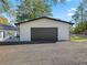 A detached garage with a black door and light-colored exterior, surrounded by a gravel driveway and landscaping at 965 Nw 73Rd Ter, Ocala, FL 34482