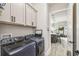 Modern laundry room featuring gray cabinets and blue washer and dryer; open view into the nearby kitchen and living space at 4522 Shockoe Cir, The Villages, FL 32163