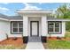 Close-up of the home's entryway with a bright white door, modern black accents, and trimmed shrubs at 55 Locust Loop Cir, Ocala, FL 34472