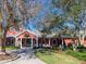 Community center featuring a red exterior, rocking chairs on the porch, a well-manicured lawn and mature landscaping at 8990 Se 178Th Muirfield Pl, The Villages, FL 32162