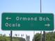 A green street sign pointing towards Ormond Beach and Ocala under a clear blue sky at 13099 Ne 7 Loop, Silver Springs, FL 34488