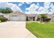 Tan one-story house with a two-car garage and lush green lawn at 17606 Se 93Rd Butler Ct, The Villages, FL 32162