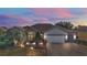 Inviting single-story home with manicured landscaping, paver driveway, and an attached two-car garage at dusk at 13077 Se 86 Ct, Summerfield, FL 34491