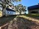 Backyard view of detached garage and home surrounded by grass and mature trees at 6701 Se 99Th Pl, Belleview, FL 34420