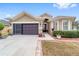 Tan house with brown doors, landscaping, and a two-car garage at 7358 Sw 101St Ave, Ocala, FL 34481