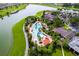 Aerial view of a luxurious community pool with a lake, surrounded by lush landscaping, palm trees, and amenities at 7387 Sw 99Th Ct, Ocala, FL 34481