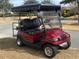 A sleek, red golf cart with a black canopy, parked on a sunny day, perfect for leisurely rides around the community at 7387 Sw 99Th Ct, Ocala, FL 34481