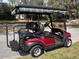 Rear side view of a red golf cart with a comfortable black seat and sunshade parked on a grassy lawn at 7387 Sw 99Th Ct, Ocala, FL 34481