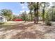 A spacious backyard showcases mature trees and leads to a striking red outbuilding against a clear blue sky at 7670 Se 110Th Street Rd, Belleview, FL 34420