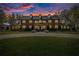Stately two-story brick home featuring a circular driveway, manicured lawn and mature trees, warmly lit at twilight at 4940 E Fort King St, Ocala, FL 34470