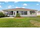 Back of house featuring screened lanai with patio chairs, well-kept lawn, and mature landscaping with an awning covered window at 13187 Se 93Rd Terrace Rd, Summerfield, FL 34491