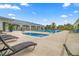 A large pool area featuring lounge chairs, lush tropical landscaping, and a white clubhouse with covered patio under a sunny sky at 7451 Sw 111Th Pl, Ocala, FL 34476