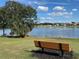 A serene lake view from a bench with lush greenery and houses in the distance, under a partly cloudy sky at 17608 Se 121St Cir, Summerfield, FL 34491